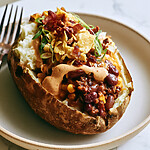 Cowboy Stuffed Baked Potatoes with Crispy Bacon Skins A baked russet potato overflowing with beef, pinto beans, corn, chipotle crema, and crushed corn chips on a plate