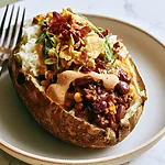 Cowboy Stuffed Baked Potatoes with Crispy Bacon Skins A baked russet potato overflowing with beef, pinto beans, corn, chipotle crema, and crushed corn chips on a plate