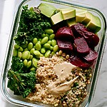 1 glass meal prep containers filled with kale, quinoa, edamame, beets, and avocado topped with hummus dressing