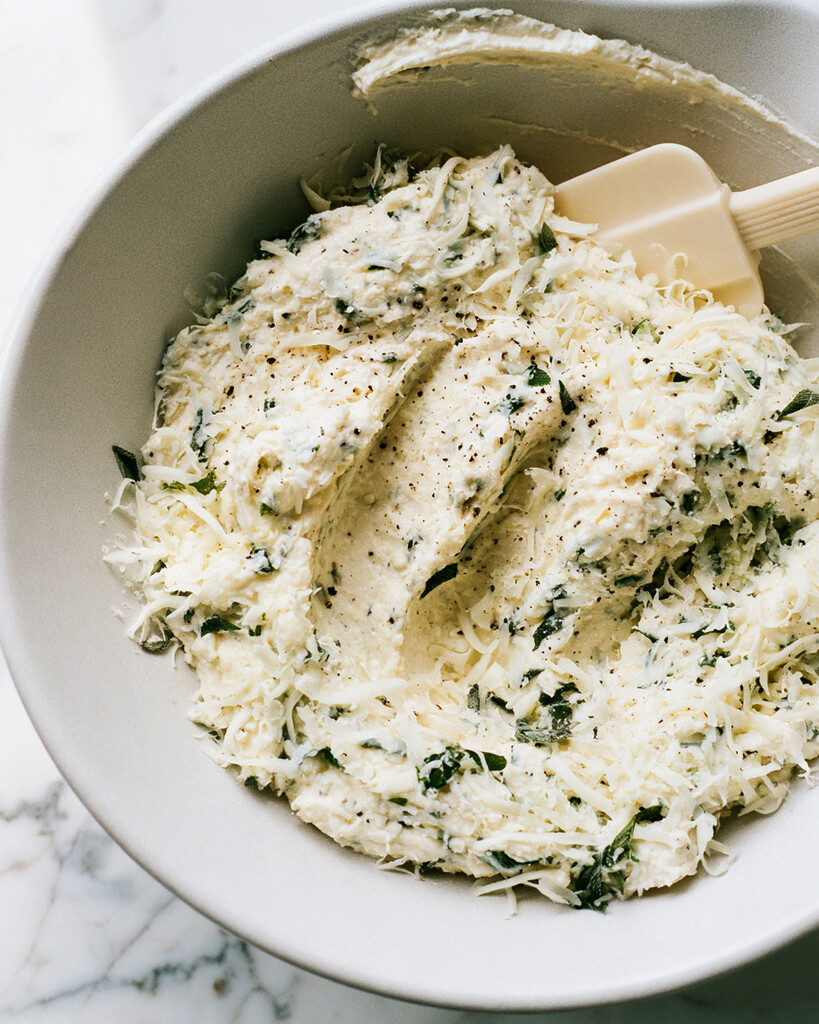 Creamy ricotta and mozzarella filling speckled with chopped sage in a metal mixing bowl