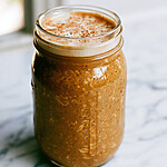 A sealed glass jar showing a thick bottom layer of spiced oats topped with white foam and a dusting of cinnamon