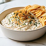 French onion dip in a ceramic bowl sitting next to wavy potato chips