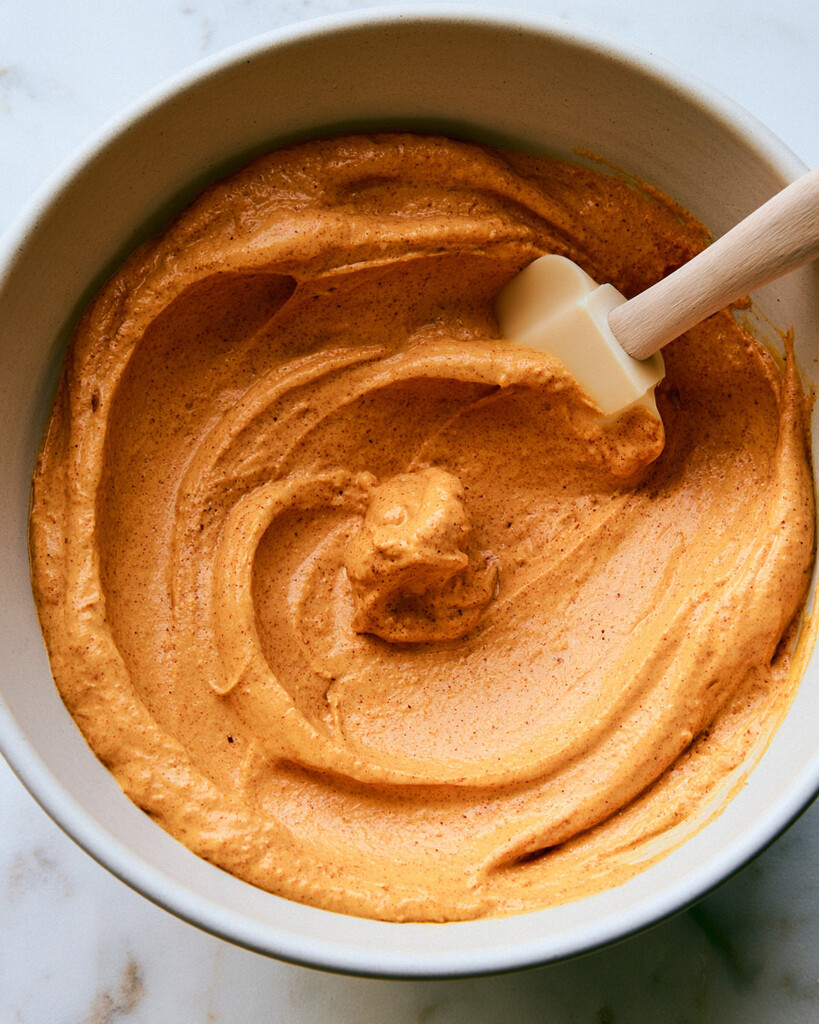 Silicone spatula mixing smooth orange pumpkin mascarpone cream in a bowl