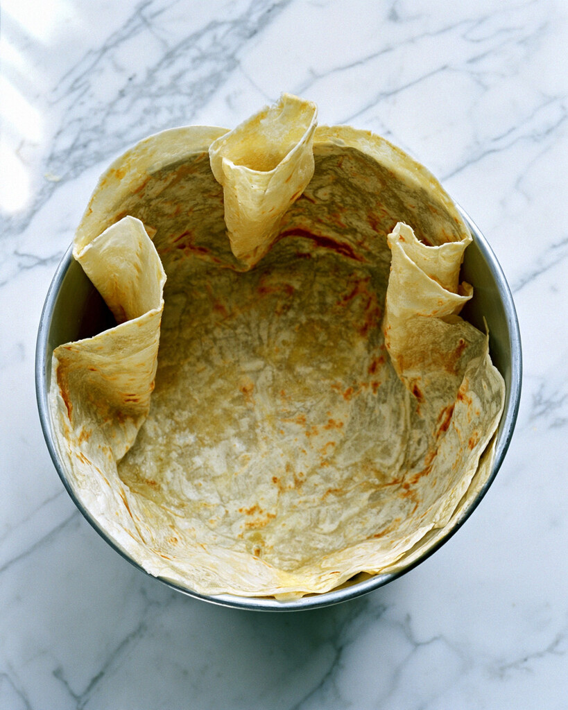 Pressing a flour tortilla into a round baking pan to form a pleated crust
