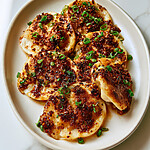 Close up of pan-fried open-faced gyoza with golden crisp edges, topped with bright red chili crisp