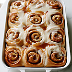 Apple Cinnamon Rolls with a Heavy Cream Soak Golden baked apple cinnamon rolls packed in a white dish, topped with icing and caramel lines