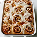 Apple Cinnamon Rolls with a Heavy Cream Soak Golden baked apple cinnamon rolls packed in a white dish, topped with icing and caramel lines