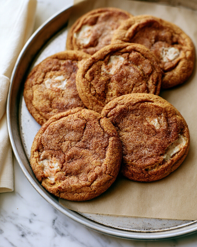 Baked pumpkin snickerdoodles resting on a lined tray with crackled tops and golden edges