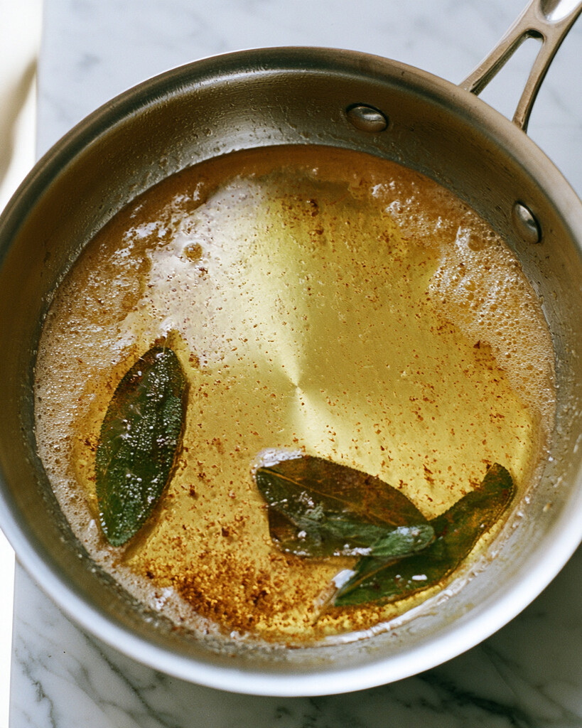 Melted butter bubbling in a small metal skillet with dark green crispy sage leaves
