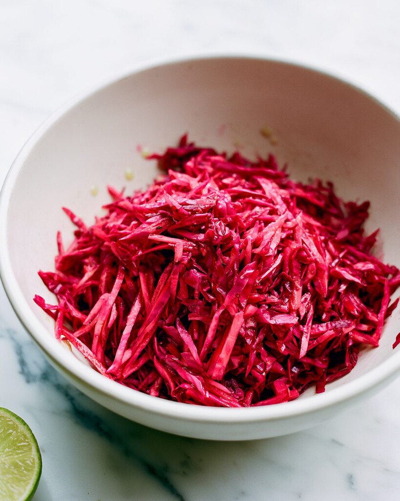 Shredded red cabbage tossed with lime juice in a white bowl