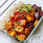 Grilled teriyaki tofu, charred pineapple, and vegetables layered over rice in a glass bowl
