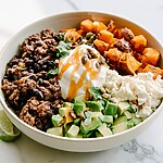 A single hot honey beef and sweet potato bowl garnished with seeds, cilantro, and fresh lime juice