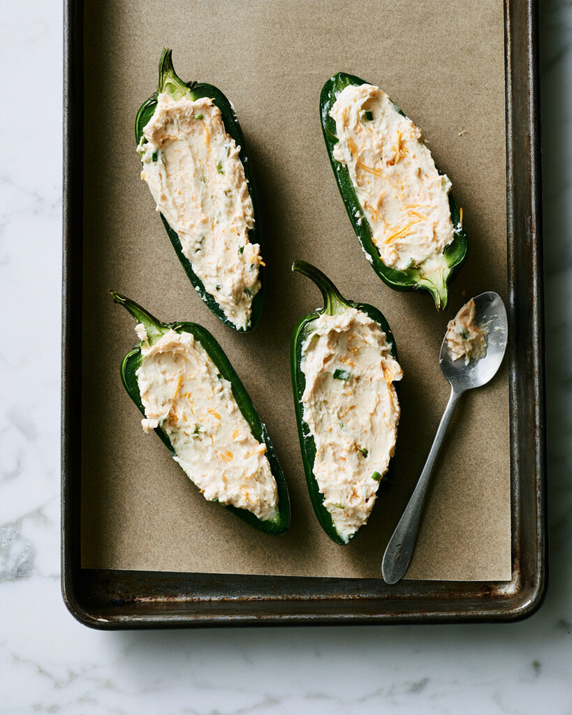 Halved jalapeños being filled with cheese mixture using a small spoon