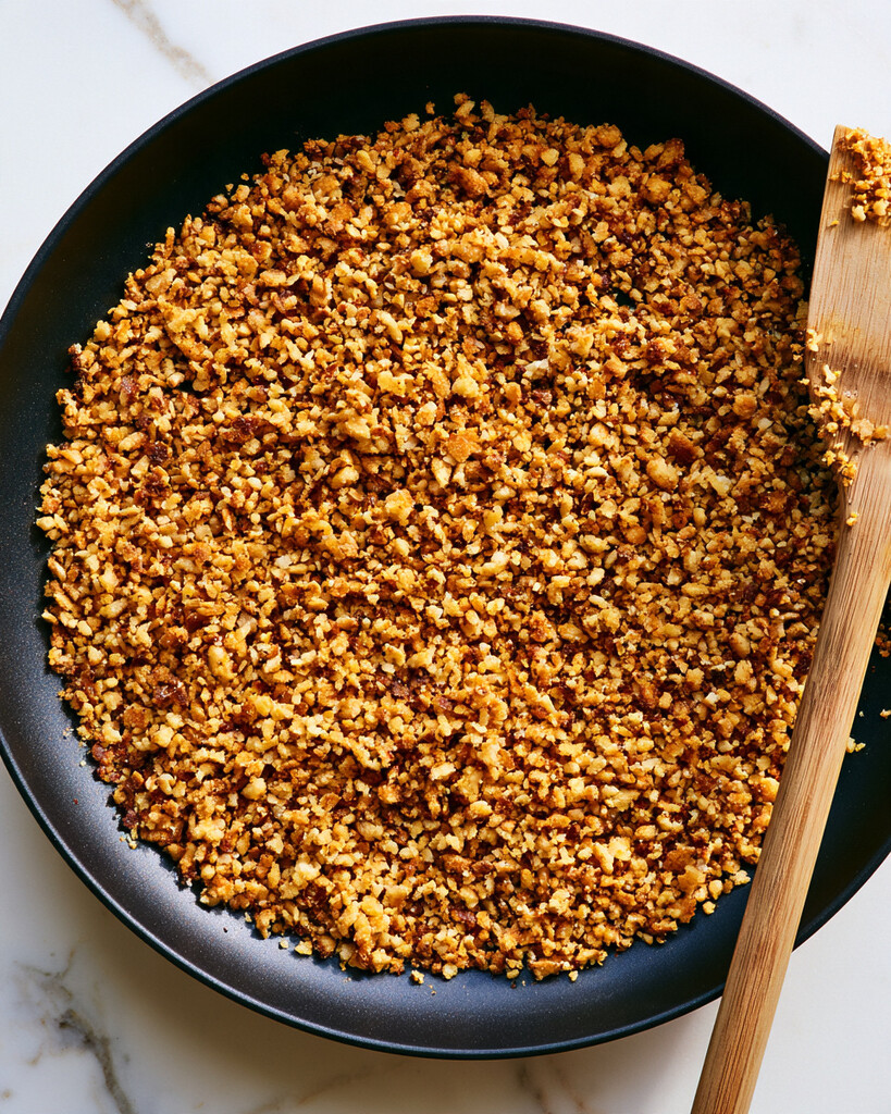 Wooden spatula stirring golden toasted panko crumbs in a black skillet