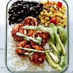 30-Minute Meal Prep Blackened Shrimp Bowls Blackened shrimp bowl ready to serve with rice, black beans, corn, and a drizzle of avocado crema