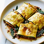 Hot Honey Brown Butter Squash Ravioli for a Pasta-Free Appetizer Three yellow squash ravioli packets topped with glossy brown butter sauce, toasted pecans, and whole sage leaves on a light plate
