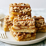 Brown Butter Apple Pie Bars with Salted Caramel Stacked brown butter apple pie bars with salted caramel on a white plate showing a thick layer of cinnamon apples