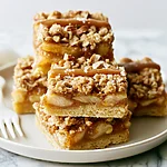 Brown Butter Apple Pie Bars with Salted Caramel Stacked brown butter apple pie bars with salted caramel on a white plate showing a thick layer of cinnamon apples