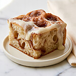 Square of cream cheese glazed cinnamon roll focaccia on a light plate with airy crumb and icing