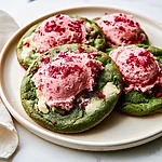 Brown Butter Matcha Cookies with Strawberry Frosting Seven brown butter matcha cookies on a light plate, topped with bright pink strawberry frosting and red freeze-dried strawberry crumbs