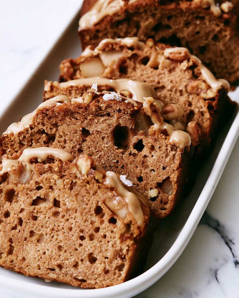 Slices of apple spice cake stacked on a white plate with glossy maple glaze