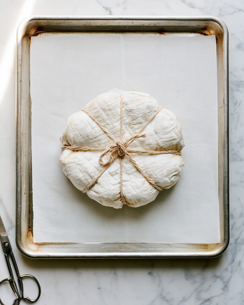 Unbaked puff pastry wrapped around brie and tied with kitchen twine into eight pumpkin segments on parchment paper