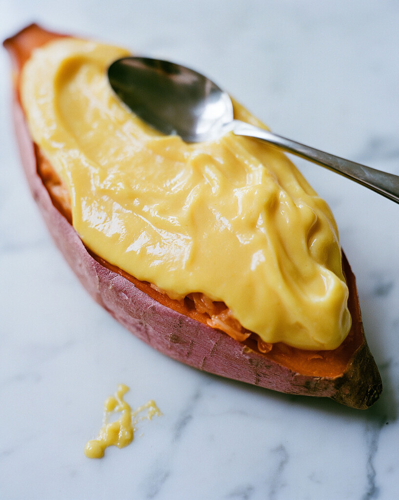 Spooning smooth yellow custard into a hollowed Japanese sweet potato half over the filling