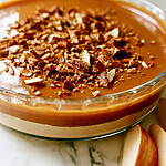 Two distinct layers of cream cheese and caramel in a glass dish topped with toffee bits and crushed pretzels