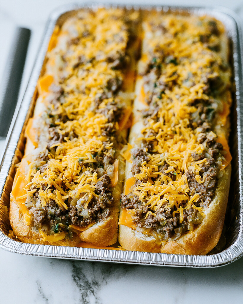 Cooked ground beef and shredded cheddar cheese layered over bottom buns in an aluminum pan