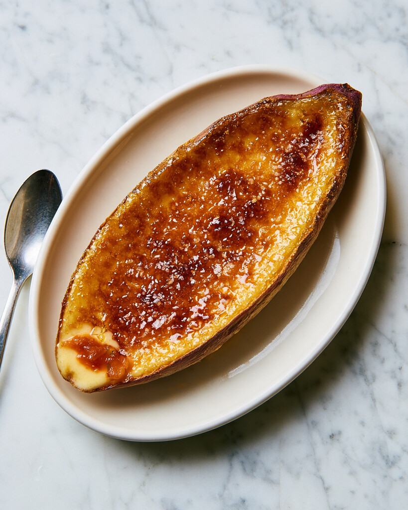 Whole Japanese sweet potato crème brûlée on a white plate topped with dark caramelized sugar and flaky sea salt